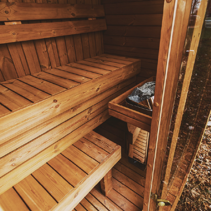 Wooden sauna with benches and a door open, showing a natural outdoor setting.